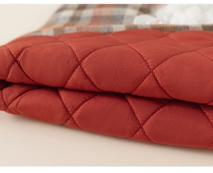 Close-up of red diamond-quilted fabric with brown plaid lining for girl's dress