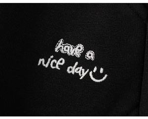 Detail of premium black knit fabric with white embroidered 'have a nice day' text and smiley