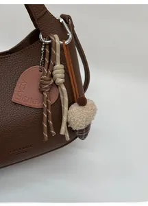 Detail view of brown pebbled leather bucket bag with heart tag and acorn pendant decoration