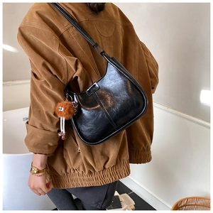 Dettaglio di una borsa a mezzaluna nera lucida con un ciondolo a mostriciattolo marrone
