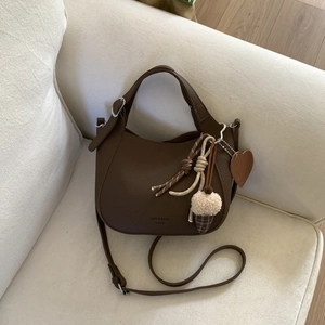 Detail of dark coffee litchi grain leather bucket bag with decorative pendants on a sofa