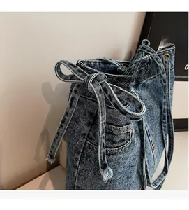 Detailed view of blue washed denim handbag with functional side pockets and bow drawstring