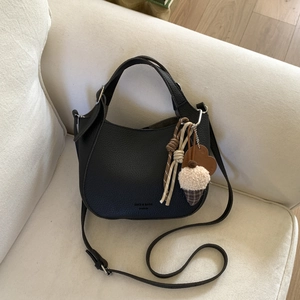 Detail of black pebbled leather hobo bag with colorful charms on a soft beige sofa