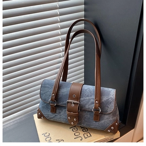 Detail of vintage blue denim underarm bag with brown leather trim and metal rivets
