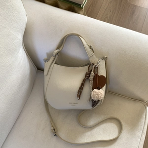 Detail of a creamy white hobo bag with litchi leather texture and stylish charms on a sofa