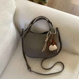 Close-up of pebble-grain shoulder bucket bag with decorative charms on a beige sofa