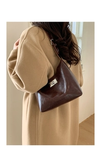 Detail of dark brown glossy leather shoulder bag with silver buckle on wool coat