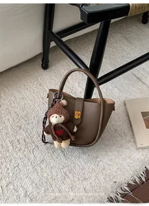 Sac seau marron en cuir grainé avec fermoir doré et charm ours en peluche sur tapis