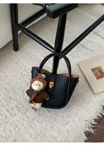 Gros plan d'un sac seau en cuir litchi noir avec boucle dorée et breloque ours en peluche