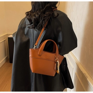 Detail view of brown matte leather bucket bag with wooden beads charm and shoulder strap