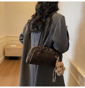 Detail of dark brown boston bag with white contrast stitching and a plush bear charm
