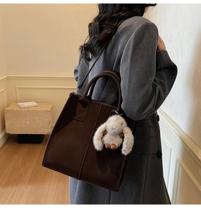 Detail view of dark brown leather tote bag with white plush rabbit pendant and long strap