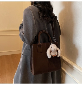 Detail of dark brown tote bag in matte leather featuring plush rabbit charm and strap