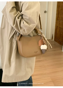Detail of a brown textured leather crossbody bag with a pinecone charm and silver hardware