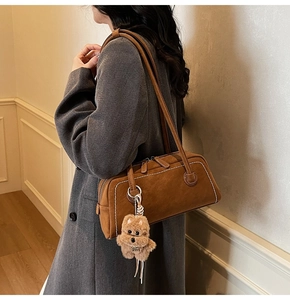 Brown suede shoulder bag with white contrast stitching and a plush puppy charm