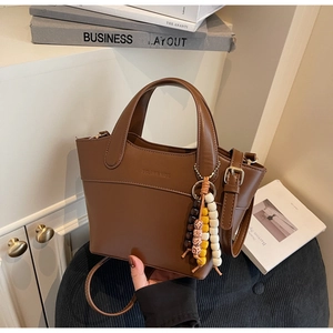 Detail view of dark brown leather bucket bag with beaded tassel and brand logo engraving