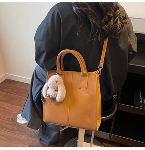 Detail of tan tote bag with symmetric stitching and a cute cream rabbit plush charm