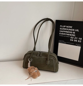 Detail view of dark green suede shoulder bag with white contrast stitching and bear charm