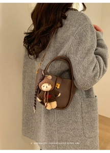 Détail d'un sac cabas rétro en cuir marron foncé avec fermoir doré et un petit ours en peluche