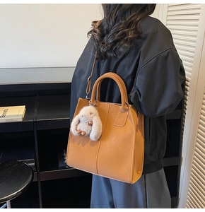 Brown faux leather tote bag with vertical stitching and cute white plush rabbit charm