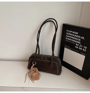 Detail of suede shoulder bag with dual zippers, white stitching and plush bear charm