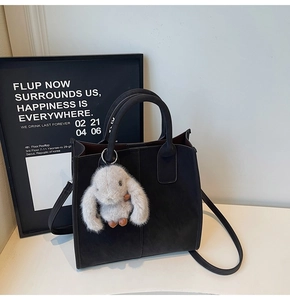 Close-up of black matte tote bag with dual handles and a grey plush bunny pendant