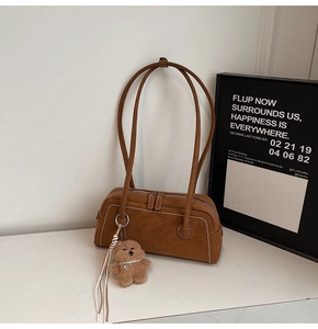Close-up of brown suede shoulder bag with white contrast stitching and a plush bear charm