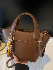 Vintage brown leather bucket bag with top handles and a colorful wooden bead charm