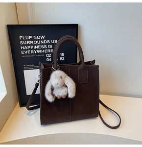 Detail of a dark brown matte leather tote bag featuring a cute grey bunny plush charm