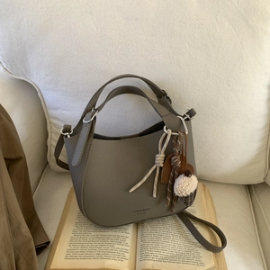 Close-up of grey leather bucket bag with plush charm on open book and beige sofa background