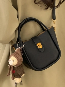 Sac seau en cuir noir grainé avec boucle dorée et charm d'ours porté par un modèle