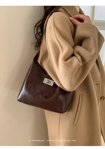 Retro dark brown glossy shoulder bag with silver metal twist lock shown on a camel coat