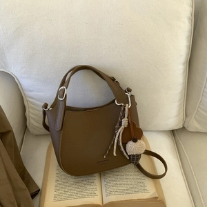 Close-up of brown textured leather bucket bag with cute plush pendant on a soft sofa