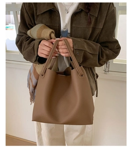 Detail of a dark brown pebble leather tote bag held by a model in a minimal setting