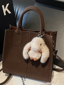 Minimalist dark brown leather tote bag with a beige rabbit fur charm and crossbody strap
