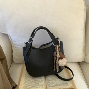 Detail of black lychee grain hobo bag with braided charms on a decorative book background