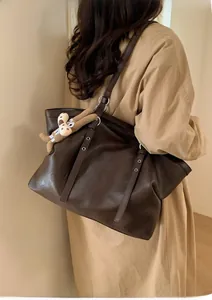 Deep brown leather tote bag with silver eyelets and plush bunny charm on trench coat
