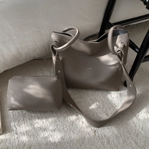 Close-up of taupe litchi grain tote bag and zipper pouch set on white carpet