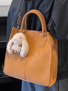 Brown faux leather tote bag with plush rabbit charm and adjustable crossbody strap