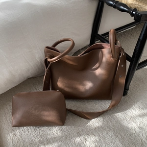 Brown grainy leather tote bag and matching pouch set on a rug in a home setting