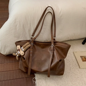 Detail of dark brown leather tote bag with silver eyelets and plush ginger man charm
