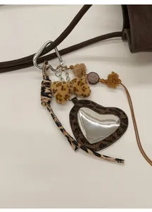 Detail of leopard print heart mirror charm and plush bow on a brown leather tote bag
