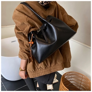 Détail d'un grand sac cabas en cuir noir avec un gland décoratif en perles de bois