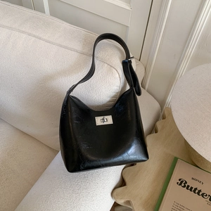 Detail of glossy black hobo bag with silver twist lock on a white textured sofa