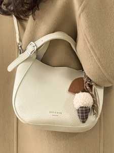 Chic cream bucket bag with litchi texture and cute charm worn over a camel wool coat