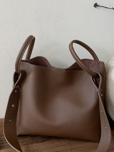 Brown litchi leather tote bag with wide rivet strap on rustic wooden tabletop