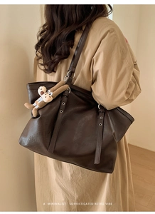 Detail view of dark brown tote bag with silver buckle and plush puppy charm on strap