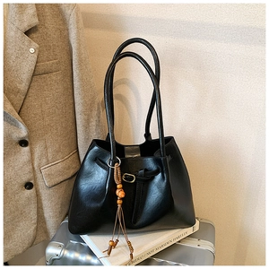 Détail du sac cabas en cuir noir avec boucle en métal et gland à franges posé sur une valise