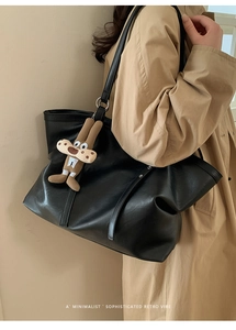 Detail of black faux leather tote bag with rivets and a cute plush charm accessory