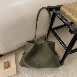 Detail of dark green leather tote bag with side pleats resting against white bedding